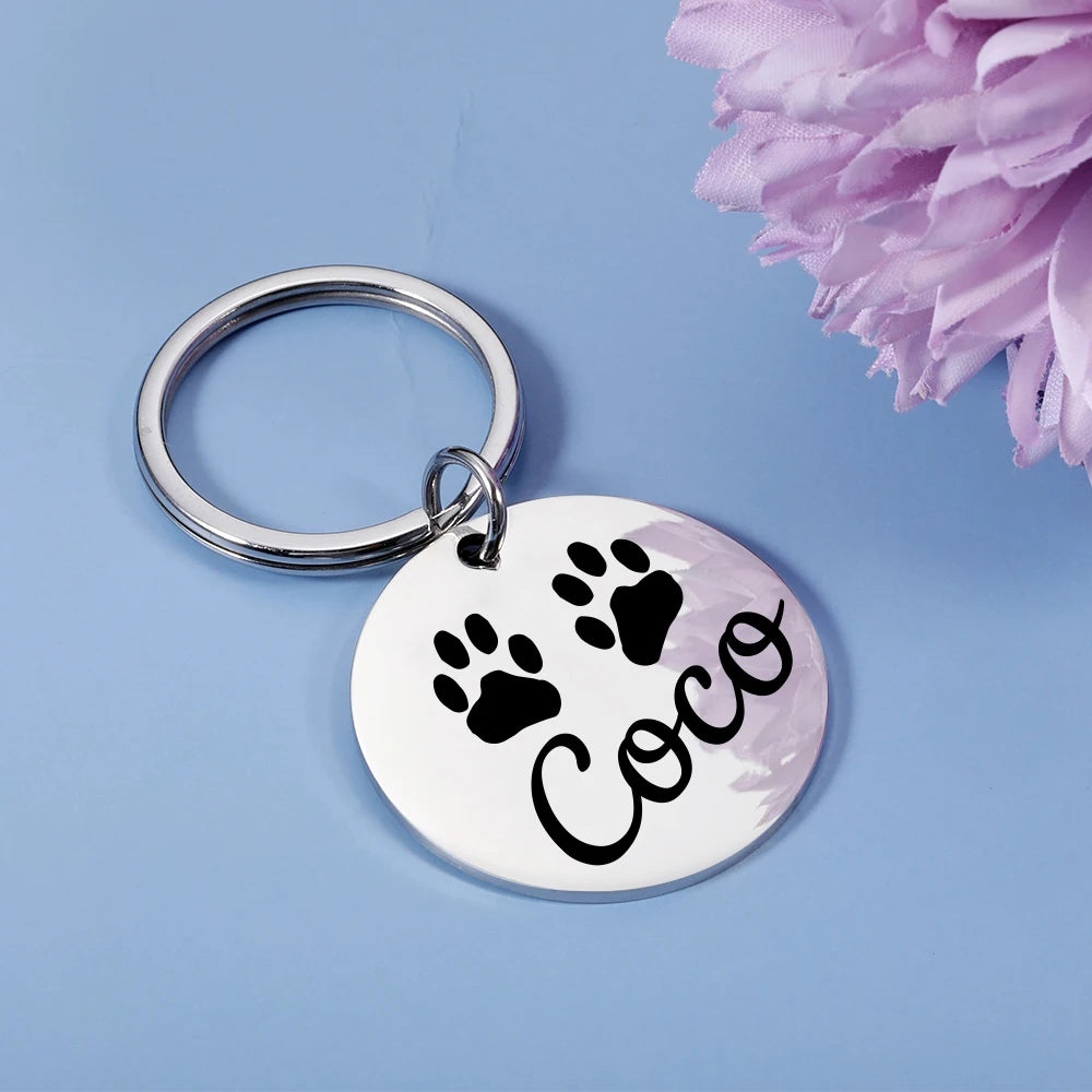 Silver round pet ID tag with paw-print design and name Coco on a keyring