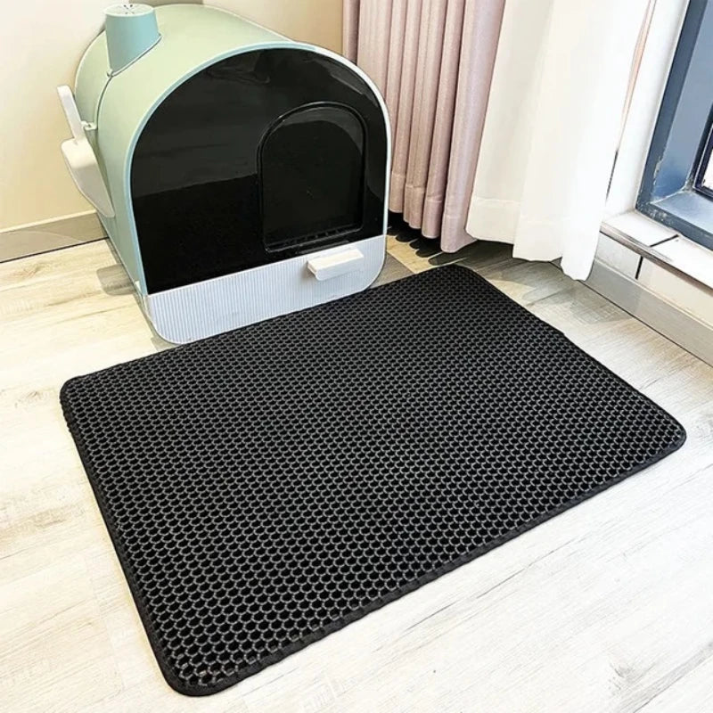 Black waterproof cat litter mat with raised lip and honeycomb texture placed in front of litter box