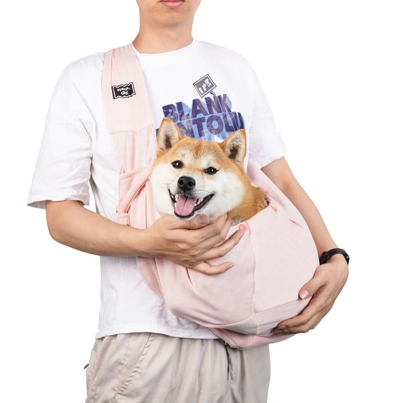 Pet sling bag with shoulder strap, light pink fabric, carrying a small dog.