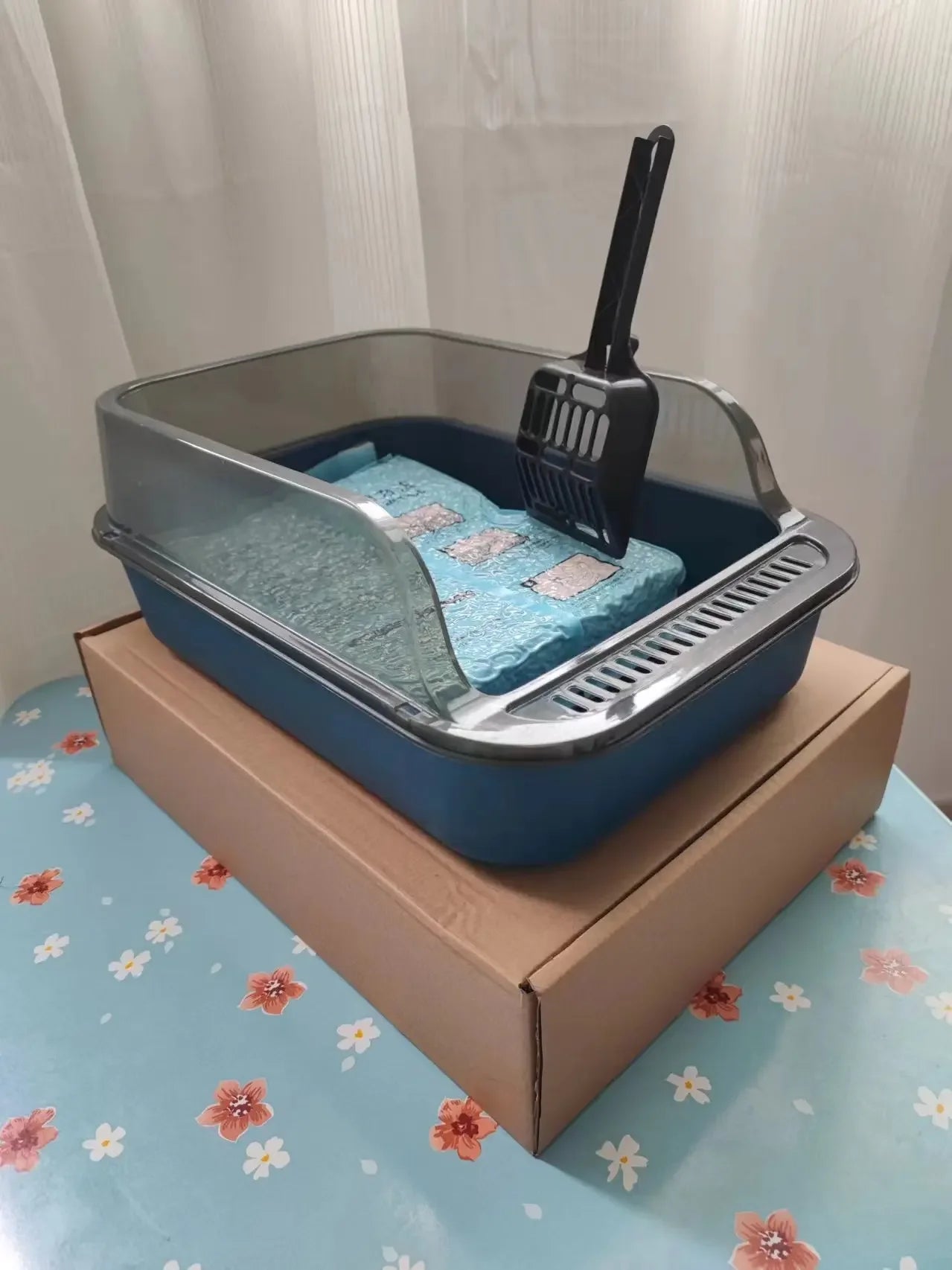 Blue semi-enclosed cat litter box with black scoop, mat, and rake panel