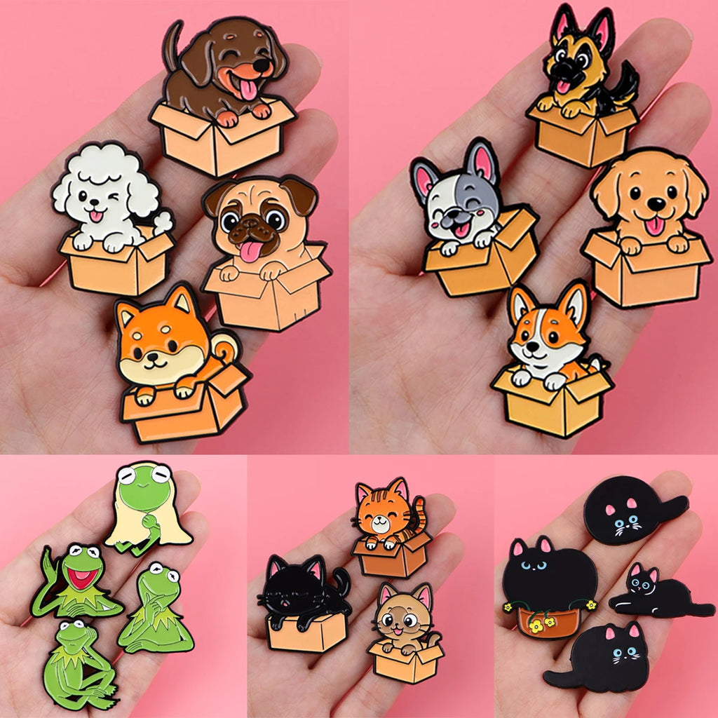 Dog and cat enamel lapel pins in open-box poses, shown on a hand