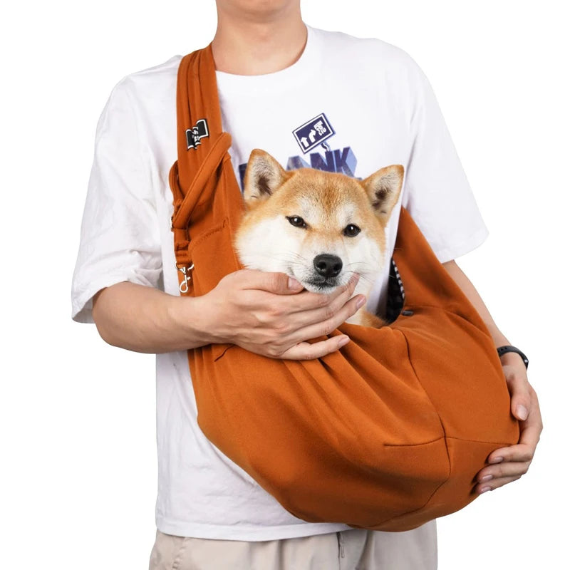 Pet sling bag with shoulder strap, orange fabric, worn while holding a small dog.