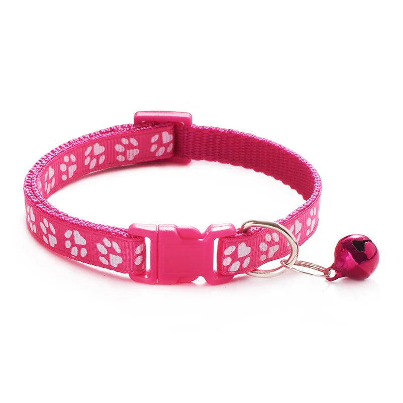 Pink paw-print cat collar with plastic buckle and bell charm on a ring