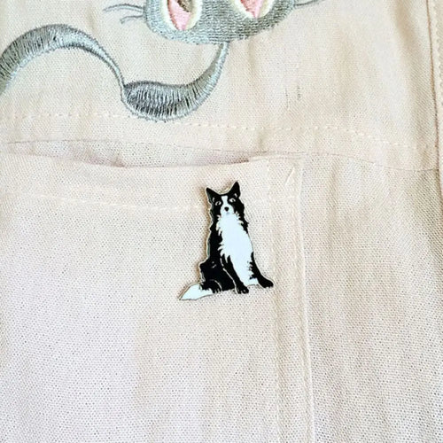 Cartoon dog enamel pin on cream shirt, small black-and-white sitting dog