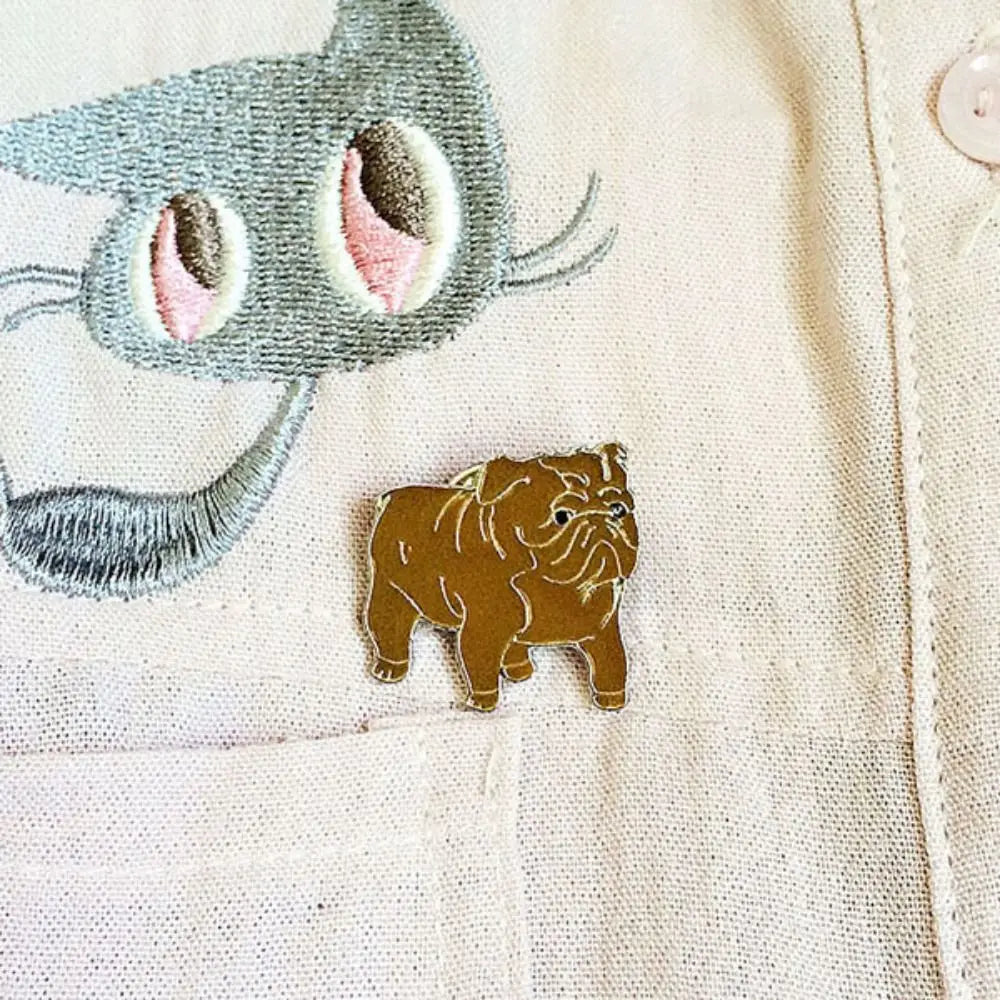 Cartoon bulldog enamel pin badge on light fabric, brown dog with white details