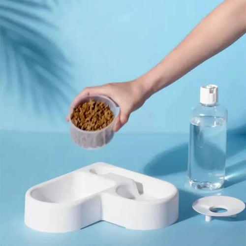 White dual pet bowl feeder with water reservoir; hand adding dry food pellets