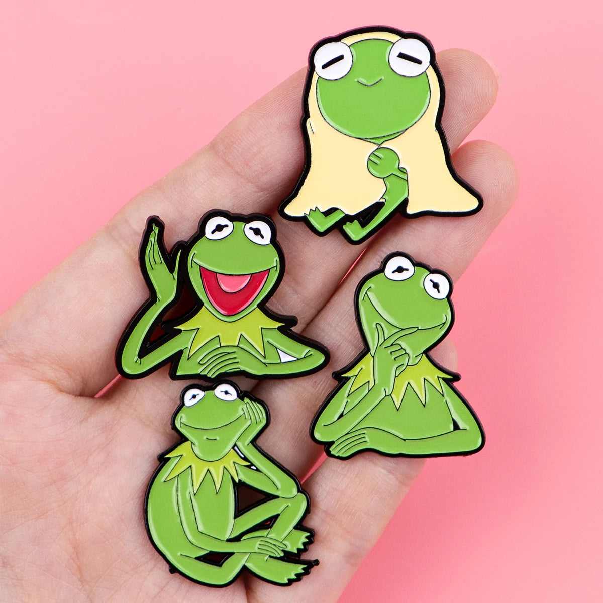 Green frog-like enamel lapel pins with animal faces, multiple pins on a hand