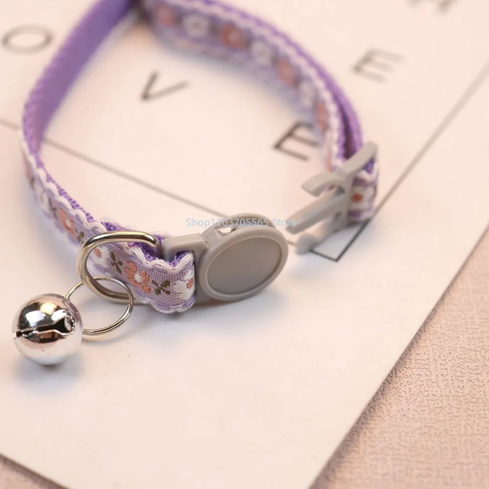 Purple floral cat collar with bell charm, round gray tag disc and metal clasp.