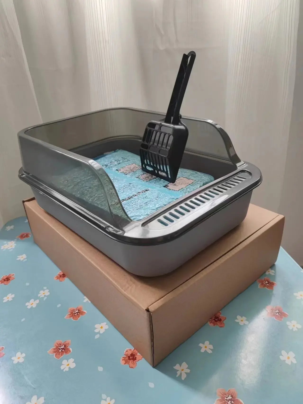 Grey semi-enclosed cat litter box with blue litter mat and black scoop
