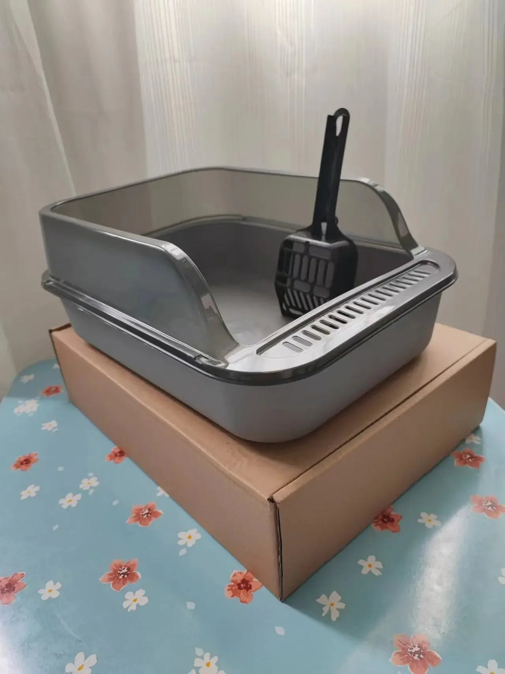 Semi-enclosed cat litter box set, gray base with scoop, on a cardboard stand