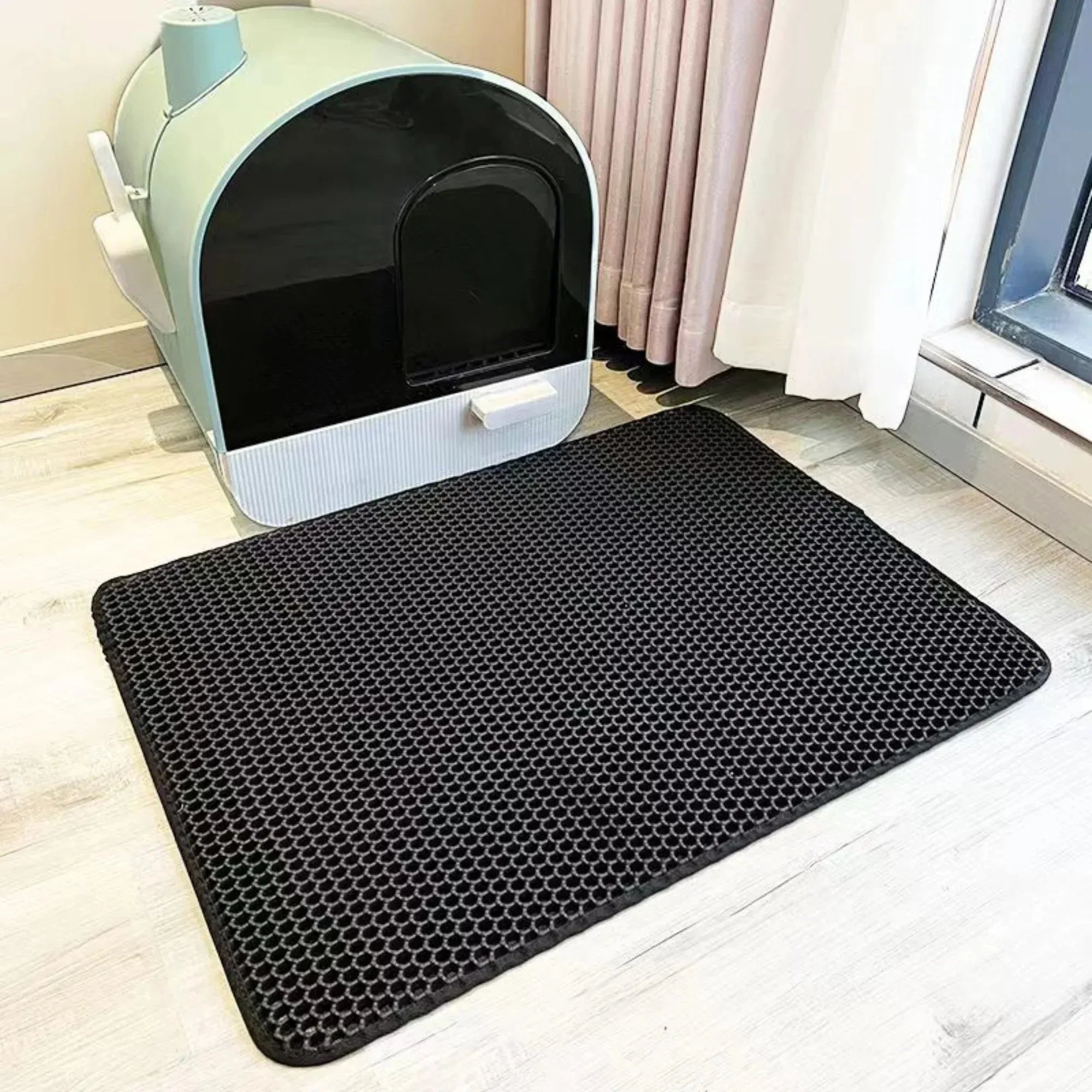 Cat litter mat with honeycomb holes, black, placed on light wood flooring
