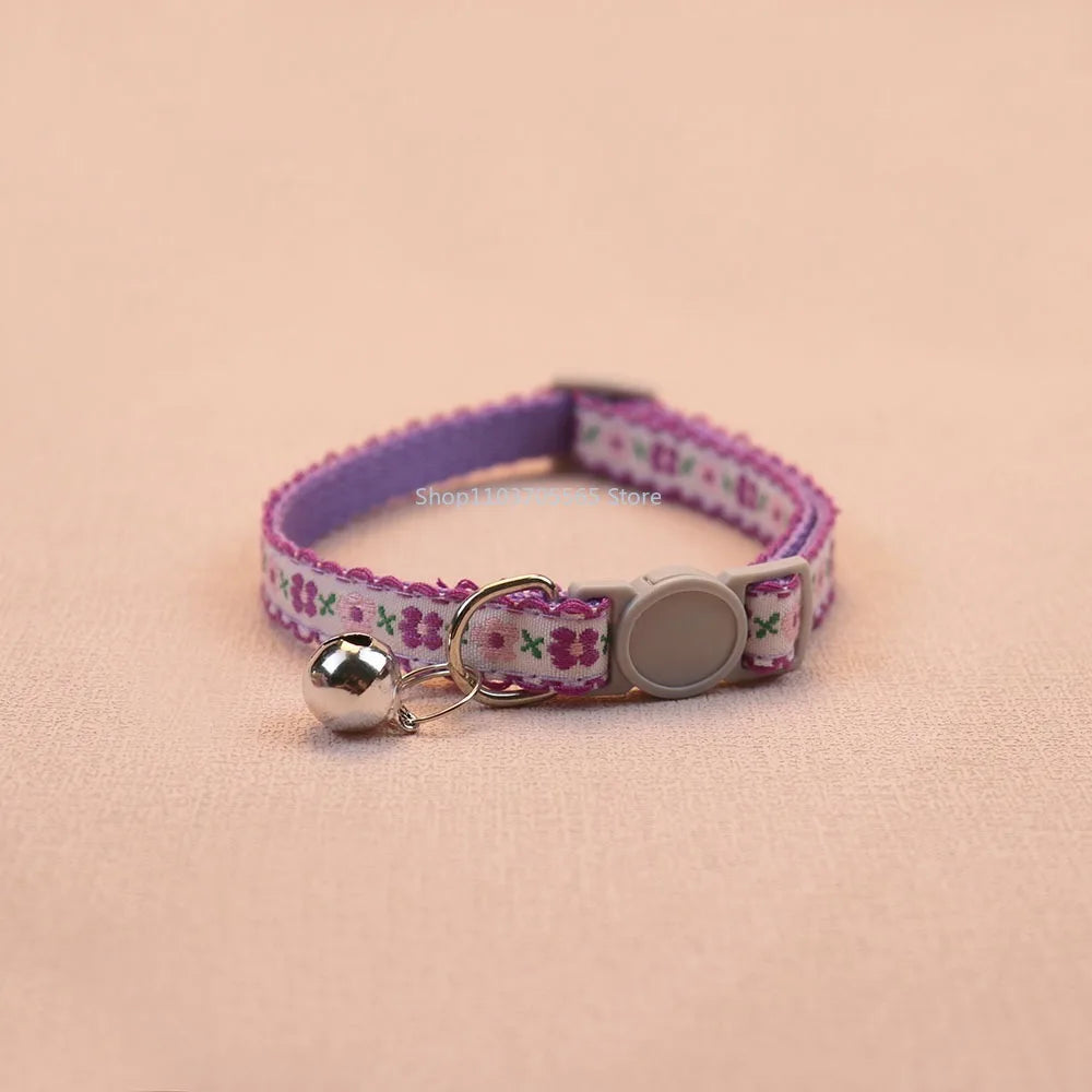 Purple floral cat collar with bell charm and round gray tag disc, adjustable buckle.