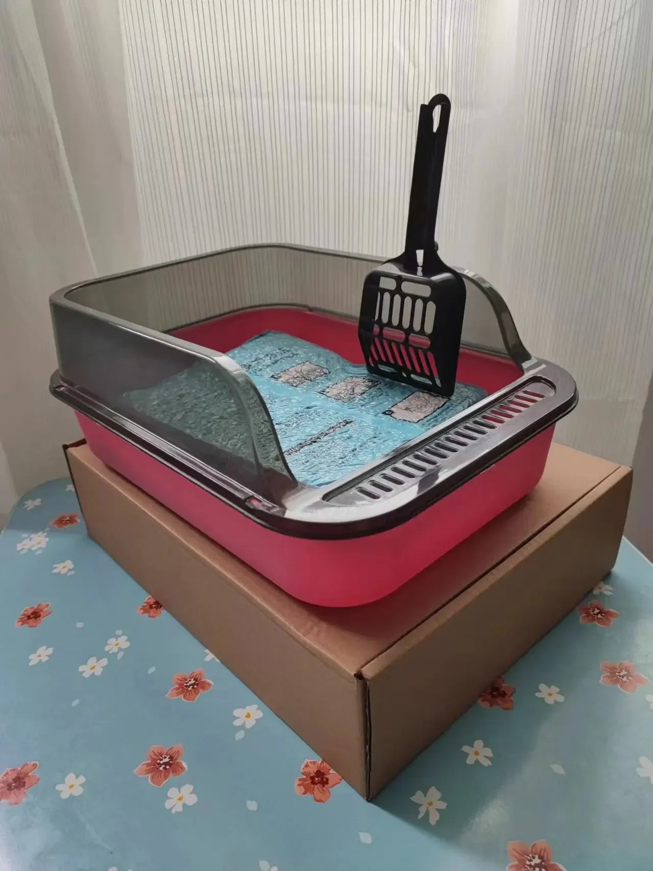 Semi-enclosed cat litter box set in pink with scoop and mat, on cardboard box