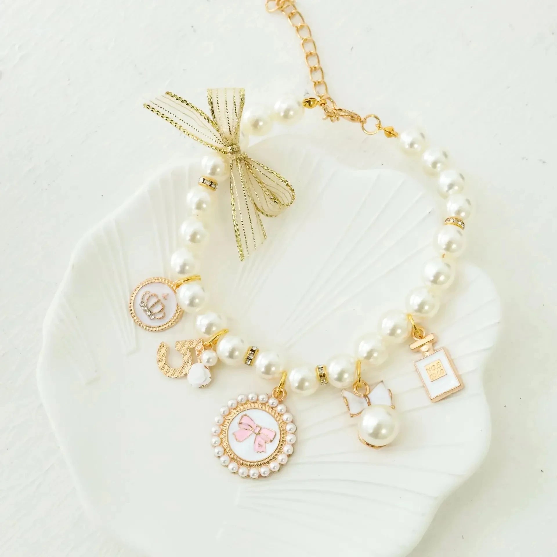 Pet pearl collar with gold charms and pink shell-style charm on a white plate