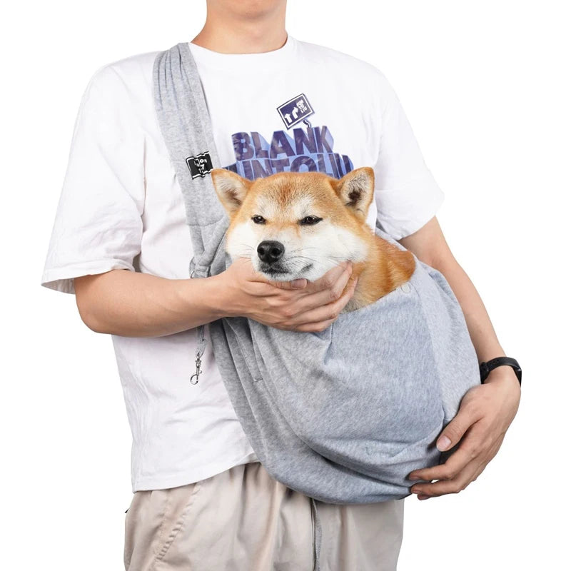 Pet sling bag with shoulder strap, light gray fabric, holding a small dog.