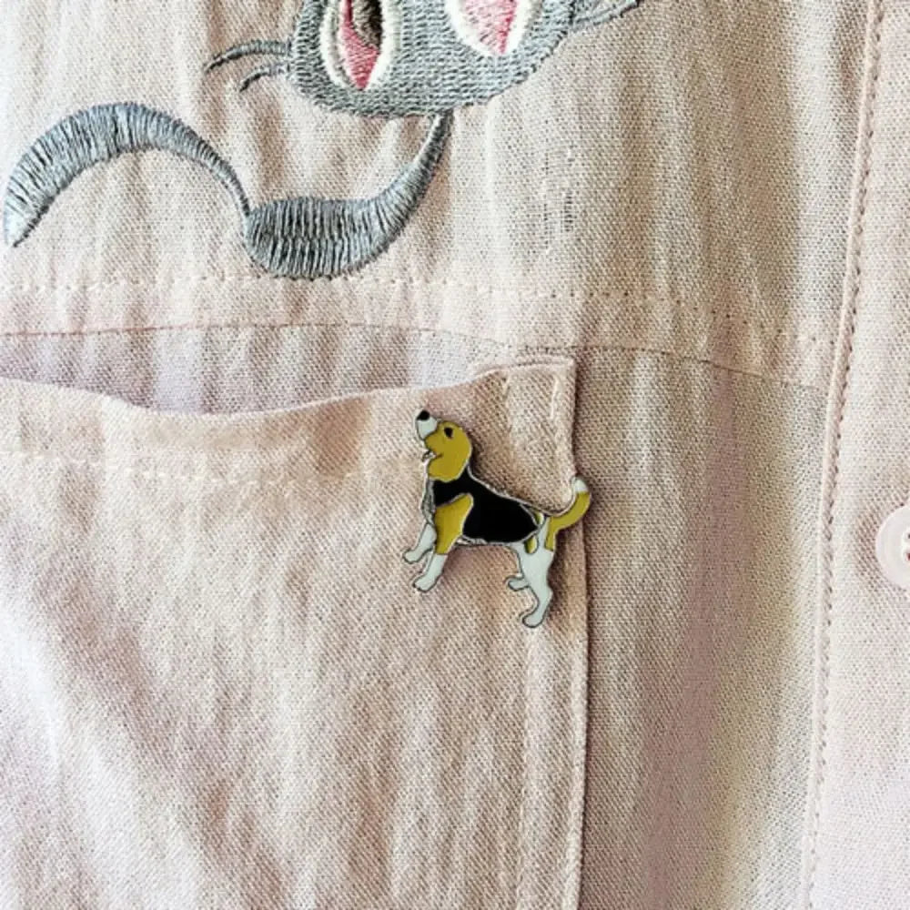 Small yellow-and-black cartoon dog enamel pin on beige fabric pocket