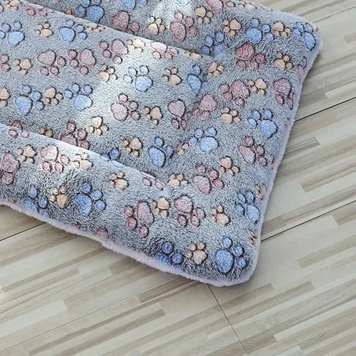 Blue plush pet blanket mat with multicolor paw-print pattern and rounded corners